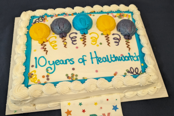 A large birthday cake iced with balloons and the words "10 years of Healthwatch"