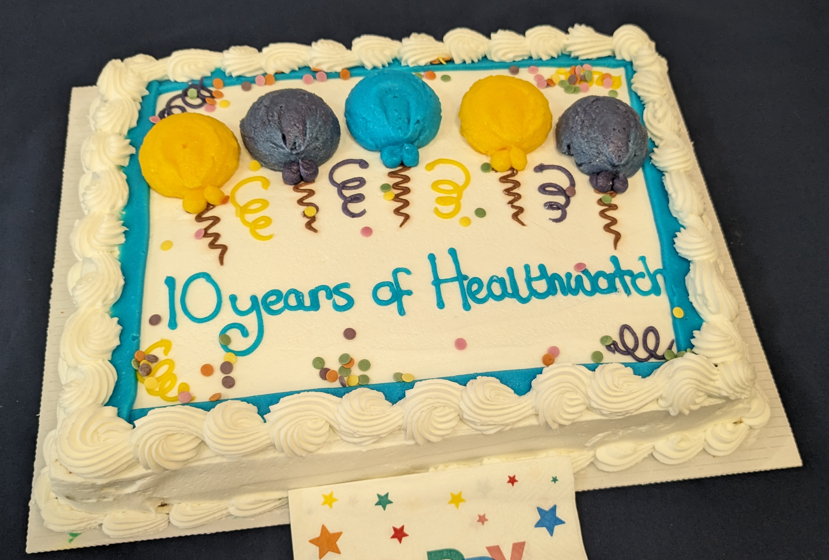 A large birthday cake iced with balloons and the words "10 years of Healthwatch"
