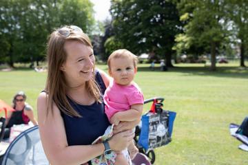 A woman holding her baby in the park. They're both smiling