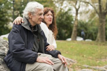 Elderly person sitting on a bench with a friend.