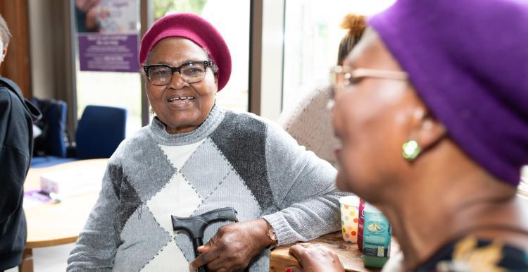Two women talking in a GP surgery waiting area.