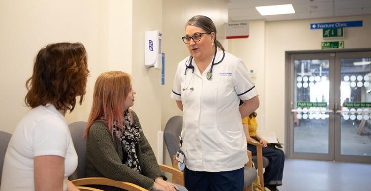 Two women speaking with a healthcare professional in a waiting room. 