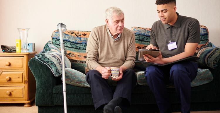 A senior man sitting with a care worker talking through treatment. 