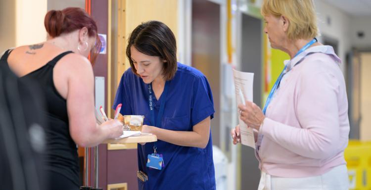 Three women in a hospital corridor filling in a form. Two are clinicians. 