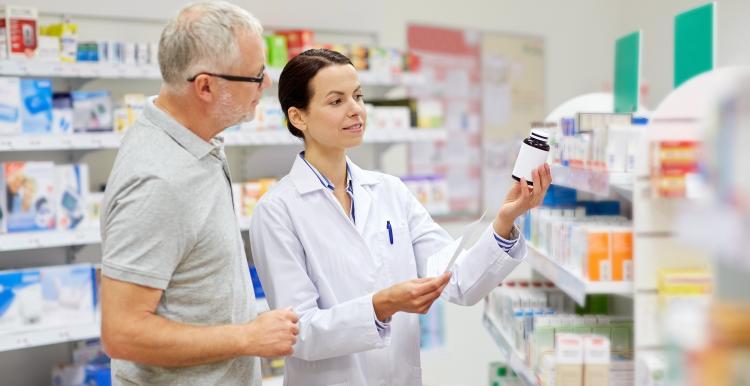 A pharmacist standing next to an older man holding a bottle of medication. 