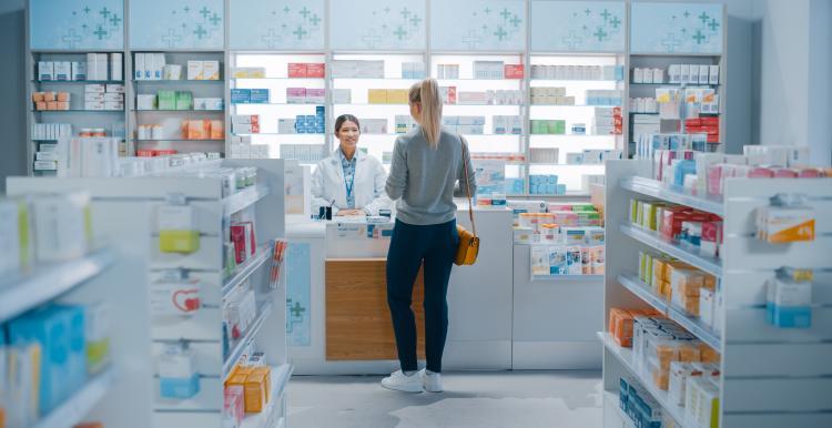 Woman stood at a pharmacy counter receiving a consultation from a female pharmacist.  