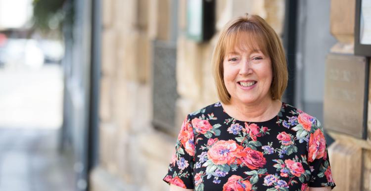 Woman standing face on looking at the camera infront of a brick wall 