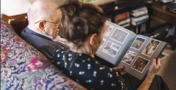 Carer and elderly man look at photo album together