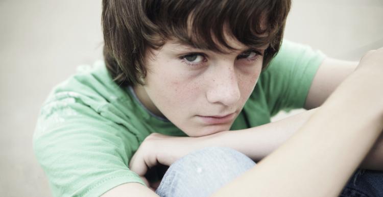 Young boy sitting down hugging his knees