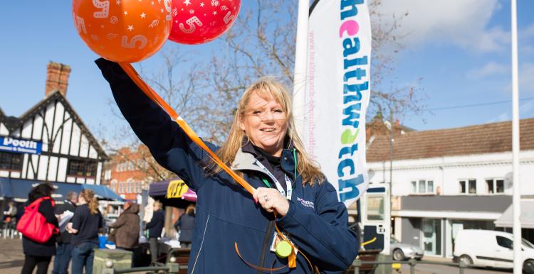 Healthwatch employee holding balloons infront of a Healthwatch sign