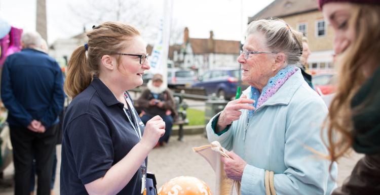 A female volunteer talking to an elderly lady at a community event. 