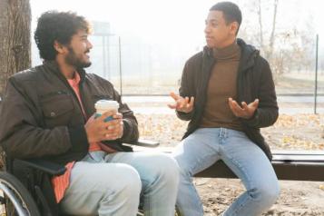 Two men sitting outside, one is in a wheelchair, talking on a wintery day. 