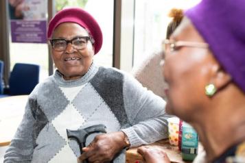 Two women talking in a GP surgery waiting area.