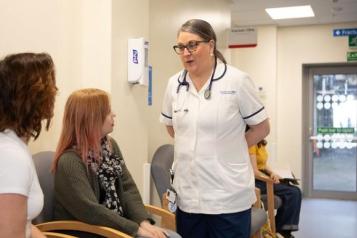 Two women speaking with a healthcare professional in a waiting room. 