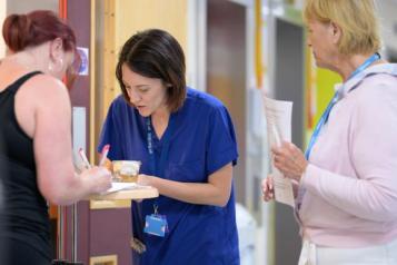Three women in a hospital corridor filling in a form. Two are clinicians. 