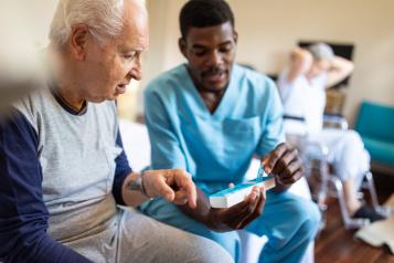 Black male nurse sitting on bed and giving instructions to senior patient when to take his medication