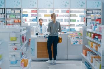 Woman stood at a pharmacy counter receiving a consultation from a female pharmacist.  