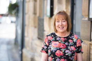Woman standing face on looking at the camera infront of a brick wall 
