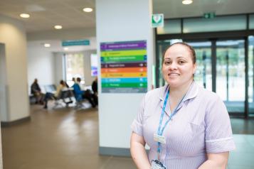 A healthcare worker standing in front of a pillar. We can see a waiting room with people behind her.