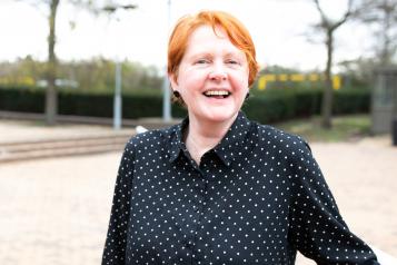 A woman with red hair stands outside laughing