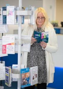 Woman standing in a GP reception area reading leaflets